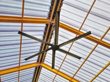 Black HVLS commercial ceiling fan mounted under metal roof structure for airport airflow control.